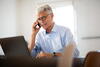 Mature man speaking on phone in plain home office